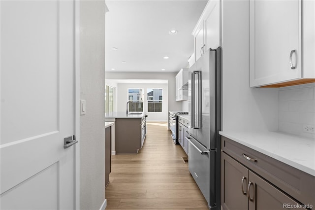 kitchen with white cabinets, tasteful backsplash, light hardwood / wood-style flooring, light stone countertops, and appliances with stainless steel finishes