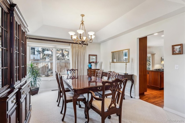 dining space featuring a chandelier, light colored carpet, and a raised ceiling