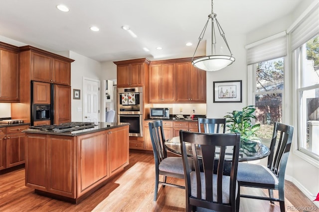 kitchen with a center island, stainless steel appliances, dark stone countertops, pendant lighting, and light wood-type flooring