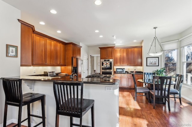 kitchen featuring pendant lighting, light hardwood / wood-style floors, a kitchen bar, kitchen peninsula, and stainless steel appliances