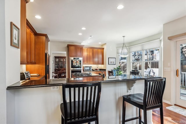 kitchen featuring stainless steel appliances, kitchen peninsula, light hardwood / wood-style floors, decorative light fixtures, and a breakfast bar