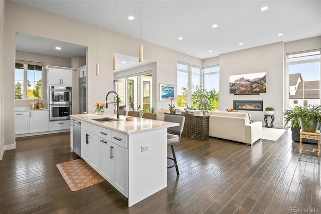 kitchen with a kitchen breakfast bar, hanging light fixtures, sink, white cabinets, and a kitchen island with sink