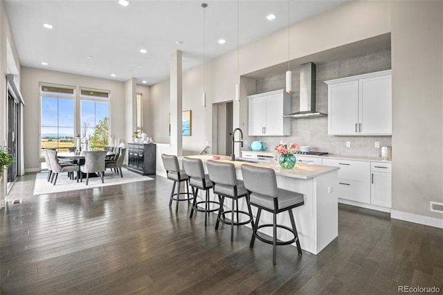 kitchen with white cabinetry, wall chimney range hood, pendant lighting, and an island with sink