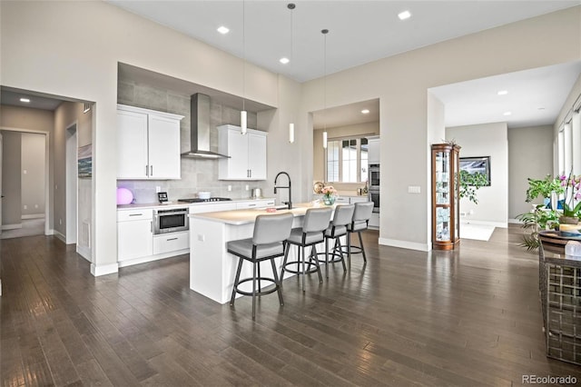 kitchen with white cabinetry, gas cooktop, wall chimney range hood, and an island with sink