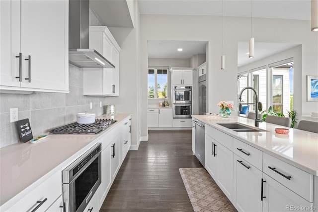 kitchen featuring pendant lighting, wall chimney exhaust hood, white cabinetry, stainless steel appliances, and sink