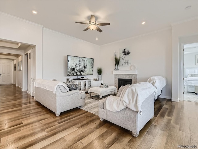 living room with hardwood / wood-style flooring, a stone fireplace, ornamental molding, and ceiling fan