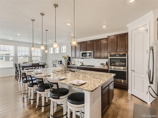 kitchen featuring sink, stainless steel appliances, an island with sink, a kitchen bar, and decorative light fixtures