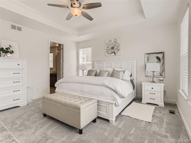 bedroom featuring ceiling fan, connected bathroom, a raised ceiling, and light colored carpet