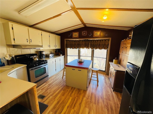 kitchen with light wood-style flooring, vaulted ceiling with beams, stainless steel range with gas stovetop, white cabinets, and under cabinet range hood