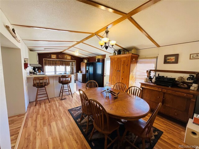 dining space featuring a textured ceiling, lofted ceiling with beams, light wood-type flooring, and a chandelier