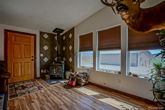 foyer entrance with a wood stove, wood finished floors, plenty of natural light, and vaulted ceiling
