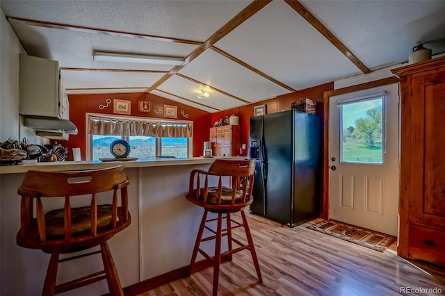 kitchen featuring a peninsula, a wealth of natural light, black refrigerator with ice dispenser, and light wood-style floors