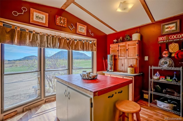 kitchen with a mountain view, light wood-style floors, tile countertops, a kitchen island, and lofted ceiling