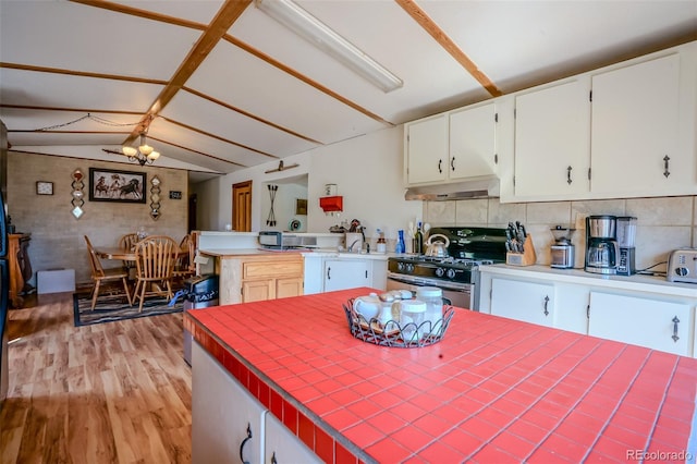 kitchen featuring stainless steel gas range oven, light wood-style flooring, under cabinet range hood, vaulted ceiling, and white cabinets
