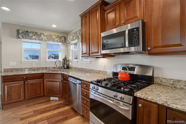 kitchen featuring light stone counters, appliances with stainless steel finishes, light hardwood / wood-style floors, and sink