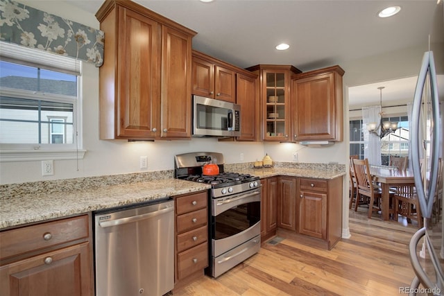 kitchen with appliances with stainless steel finishes, an inviting chandelier, hanging light fixtures, light stone countertops, and light hardwood / wood-style floors