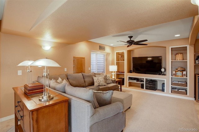 living room with built in shelves, ceiling fan, light carpet, and a textured ceiling