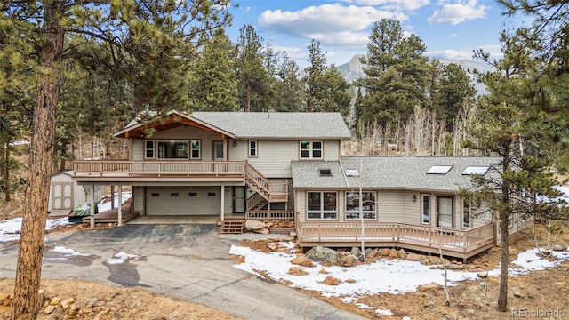 chalet / cabin with driveway, a garage, roof with shingles, a storage unit, and a wooden deck