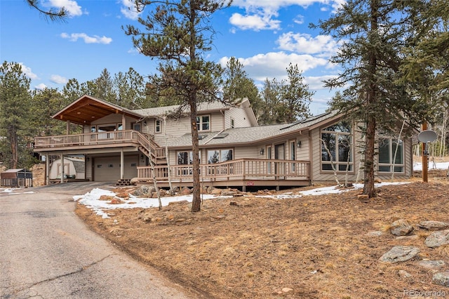 chalet / cabin featuring aphalt driveway, a deck, and an attached garage