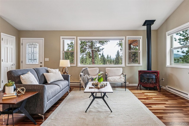 living area featuring a baseboard heating unit, a wood stove, baseboards, and wood finished floors