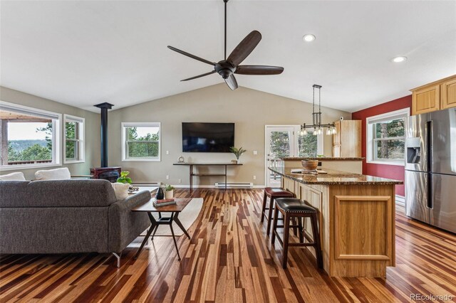 kitchen with a kitchen bar, open floor plan, stainless steel refrigerator with ice dispenser, and a wood stove