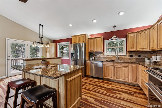 kitchen with stainless steel appliances, lofted ceiling, a sink, a kitchen island, and a kitchen bar