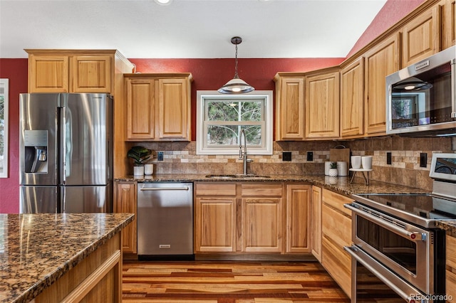 kitchen featuring a sink, hanging light fixtures, appliances with stainless steel finishes, light wood finished floors, and tasteful backsplash