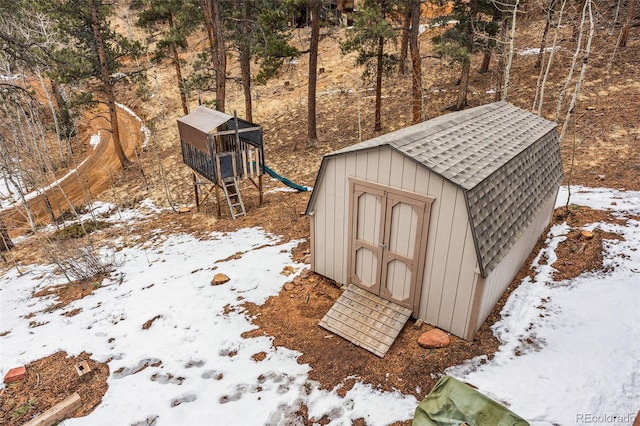 snow covered structure featuring an outbuilding, a playground, and a storage unit