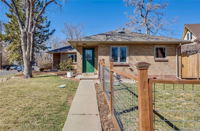 view of front facade with brick siding, fence, a front lawn, and roof with shingles