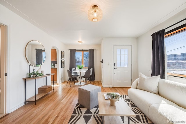 living area featuring light wood-style floors, baseboards, and arched walkways