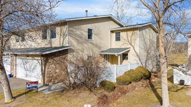 view of front of home featuring stone siding, an attached garage, fence, and driveway