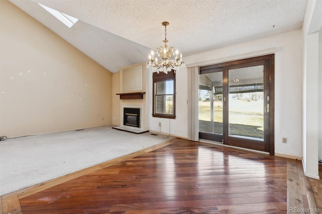 unfurnished living room with dark wood-style flooring, a glass covered fireplace, a textured ceiling, a chandelier, and vaulted ceiling with skylight