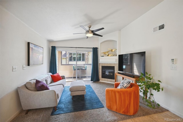 tiled living room with ceiling fan, vaulted ceiling, and a tiled fireplace