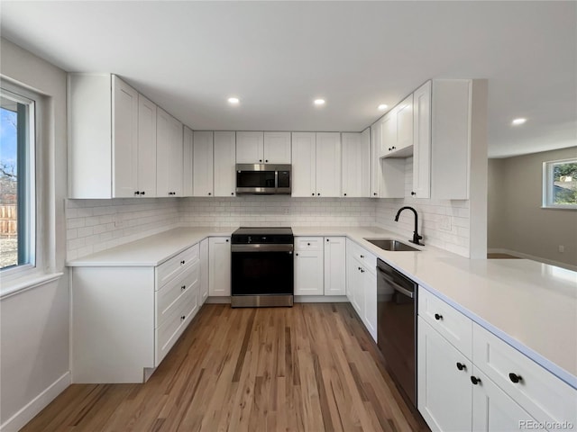 kitchen with sink, light hardwood / wood-style flooring, backsplash, white cabinets, and appliances with stainless steel finishes