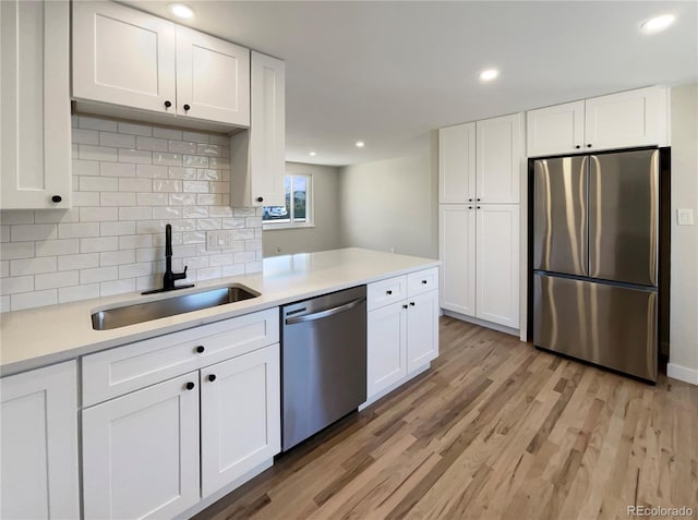 kitchen with tasteful backsplash, stainless steel appliances, sink, light hardwood / wood-style floors, and white cabinetry