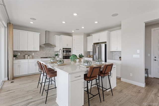 13334 Blue Amber Ct, Parker, CO 80134 - kitchen featuring stainless steel appliances, wall chimney range hood, a kitchen breakfast bar, backsplash, and light wood-style flooring