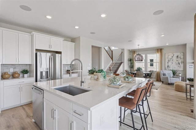 13334 Blue Amber Ct, Parker, CO 80134 - kitchen featuring appliances with stainless steel finishes, light wood-style floors, backsplash, white cabinetry, and a kitchen island with sink