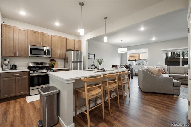 kitchen featuring appliances with stainless steel finishes, a kitchen breakfast bar, a kitchen island with sink, dark wood-type flooring, and hanging light fixtures