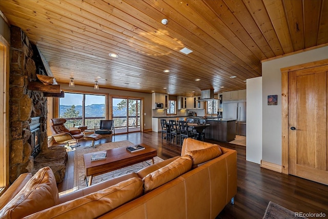 living room with a mountain view, wooden ceiling, a stone fireplace, and dark wood-type flooring