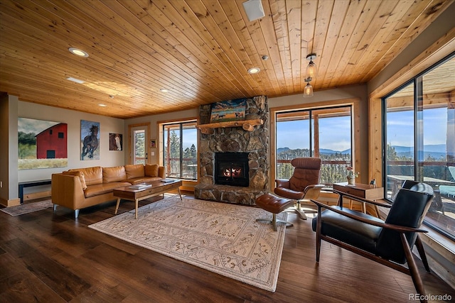 living room with a mountain view, a stone fireplace, hardwood / wood-style floors, and wooden ceiling