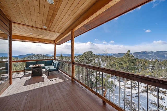 snow covered deck featuring a mountain view and an outdoor living space with a fire pit