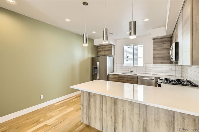 kitchen with stainless steel appliances, tasteful backsplash, light wood-style flooring, a sink, and a peninsula