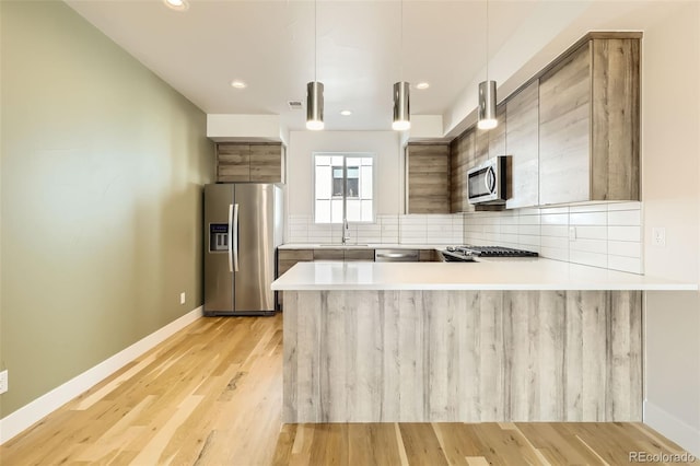 kitchen featuring backsplash, appliances with stainless steel finishes, light wood-style floors, modern cabinets, and a peninsula