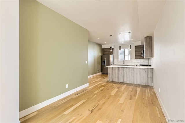 kitchen with tasteful backsplash, stainless steel fridge with ice dispenser, a peninsula, light countertops, and light wood-style floors