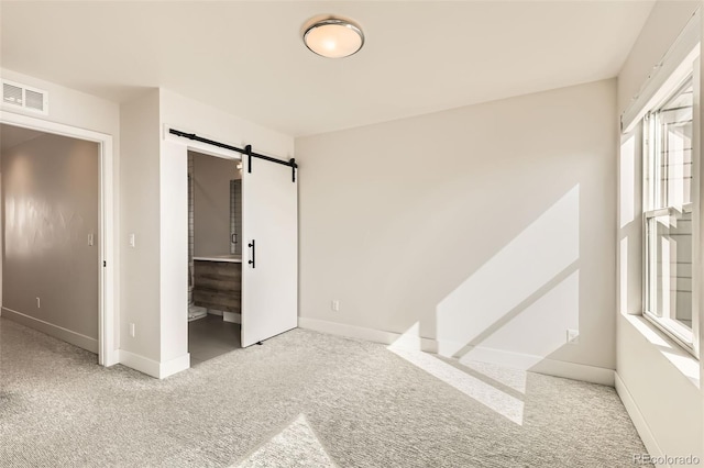 unfurnished bedroom featuring carpet, a barn door, visible vents, and baseboards