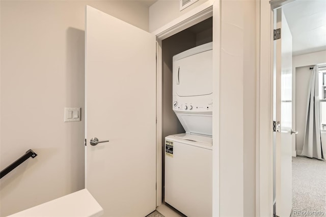 clothes washing area with stacked washing maching and dryer, visible vents, and laundry area