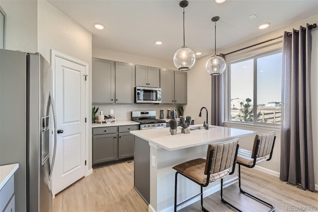 kitchen featuring an island with sink, pendant lighting, decorative backsplash, appliances with stainless steel finishes, and light wood-type flooring