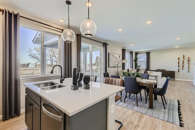 kitchen with dishwasher, sink, pendant lighting, light hardwood / wood-style floors, and a center island with sink