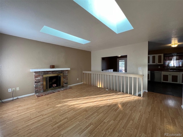 unfurnished living room with a brick fireplace, sink, hardwood / wood-style flooring, and a skylight