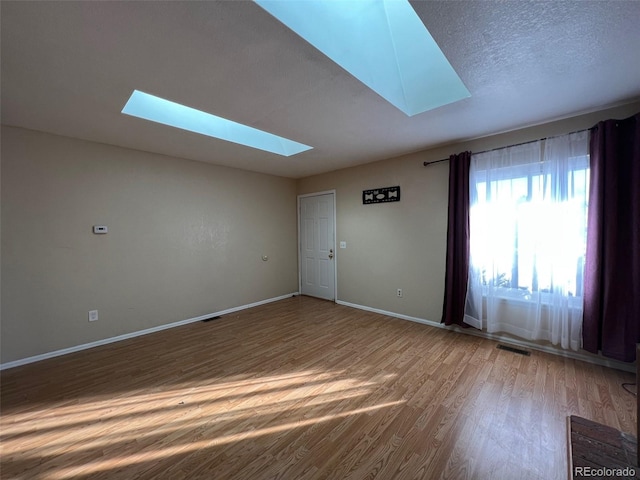 empty room with a skylight, hardwood / wood-style flooring, and a textured ceiling